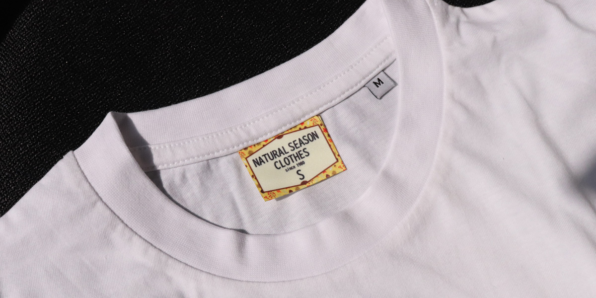 白Tシャツに縫い付けられたフルカラーのオリジナル襟タグ。ブランド名やサイズを印刷可能なハンドメイド向けネームタグ。