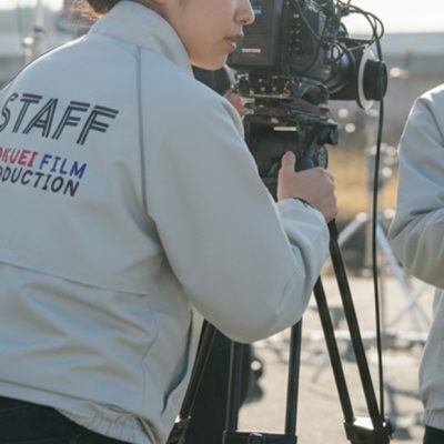 明るい屋外の撮影現場で、ロゴ入りのオリジナルブルゾンを着た画像