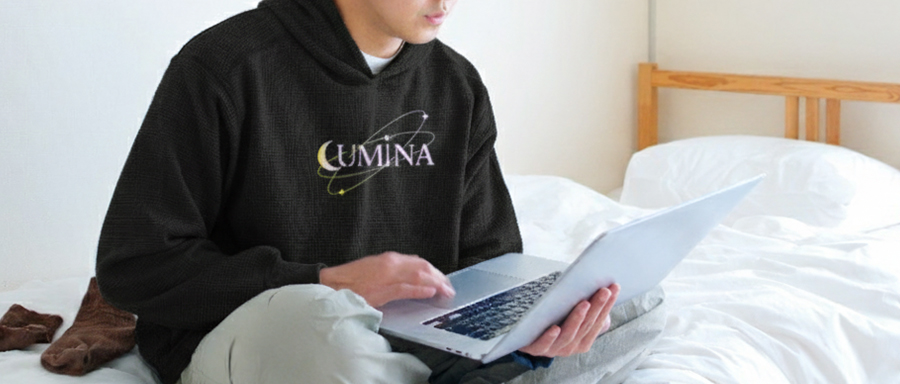 オリジナルパーカーを着用し、ベッドでノートパソコンを使う男性