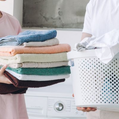 オリジナルTシャツを洗濯する夫婦（またはカップル）。女性が畳んだタオルを持ち、男性が洗濯かごを持っている様子。