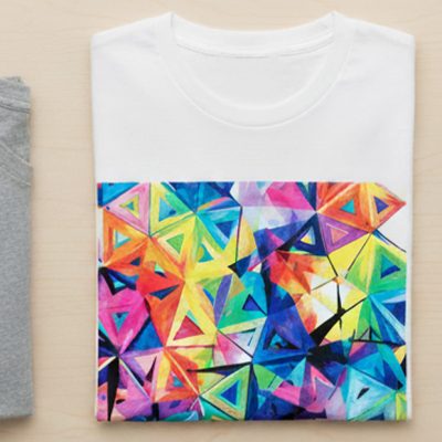 カラフルなデザインのDTFプリントTシャツ、DTFシート、数色の無地Tシャツ、そして品質やコストを象徴する虫眼鏡や電卓などが置かれている俯瞰写真。